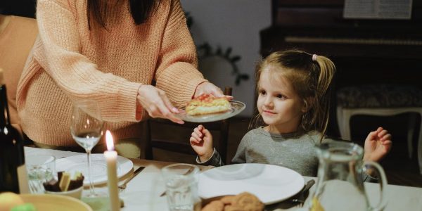 A mother serves dinner to her young daughter at a warmly lit family table, creating a cozy atmosphere.